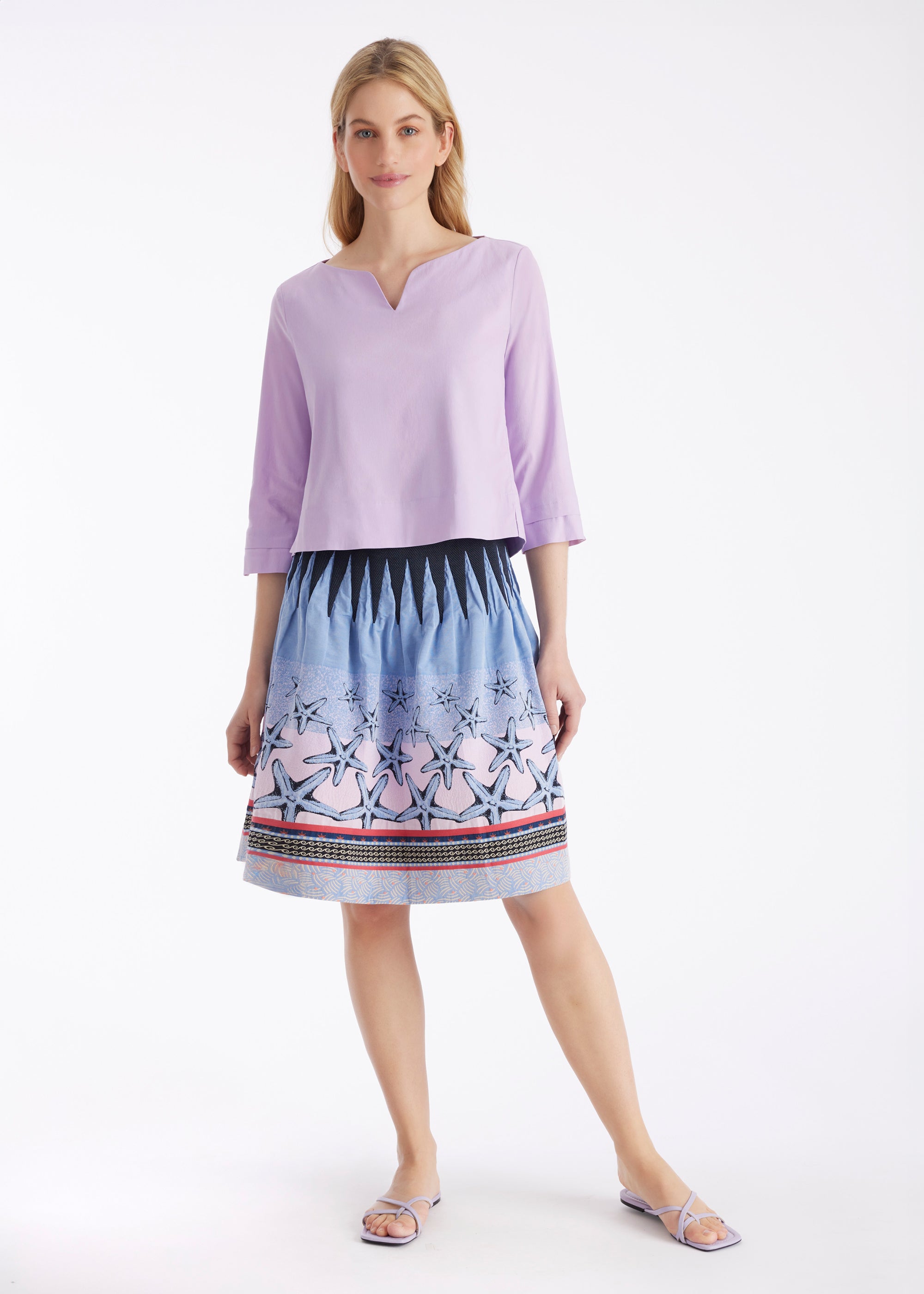 Woman models a lilac notch neck top and a blue and pink starfish print skirt.